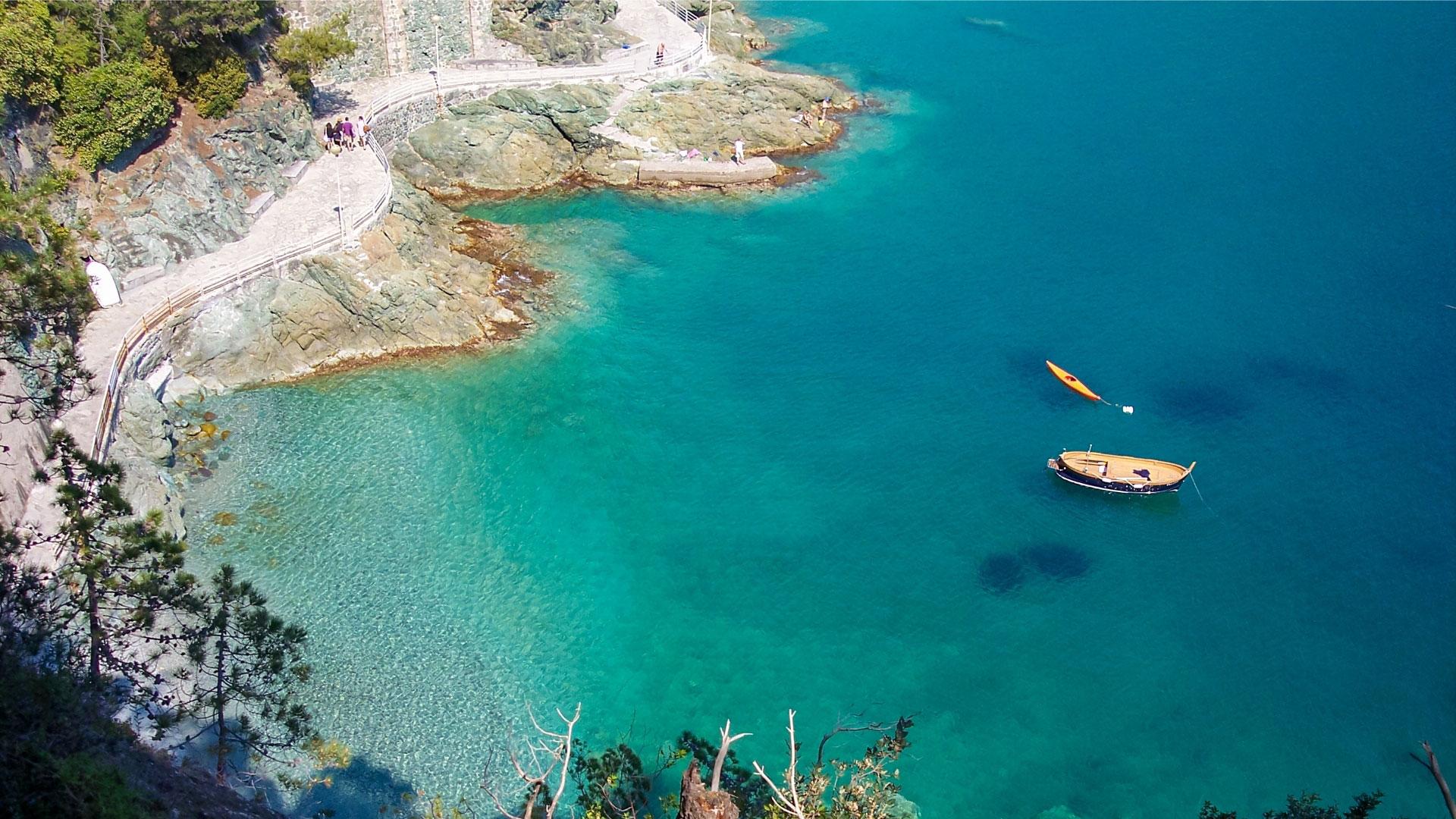 Coastal path with crystal-clear waters and floating boats.