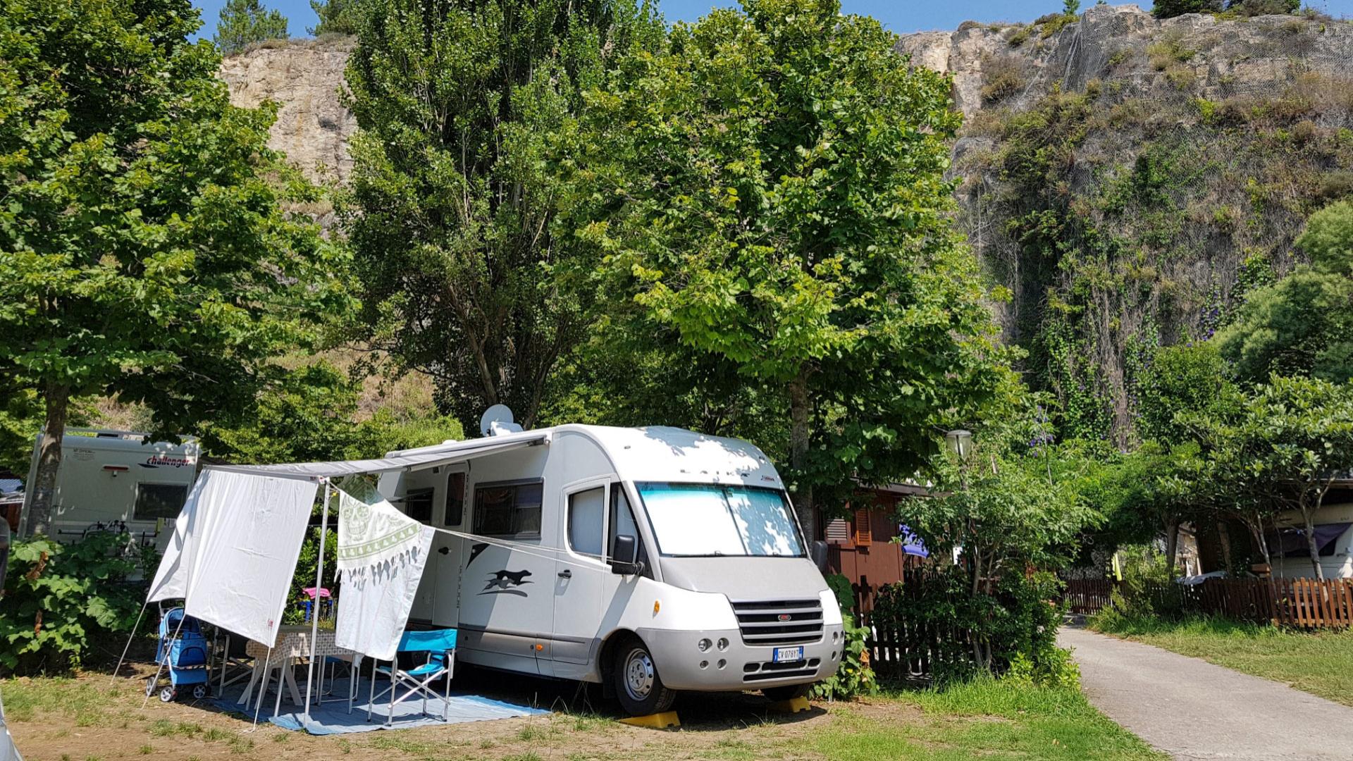 Camper parcheggiato in campeggio verde con vista su una collina rocciosa.