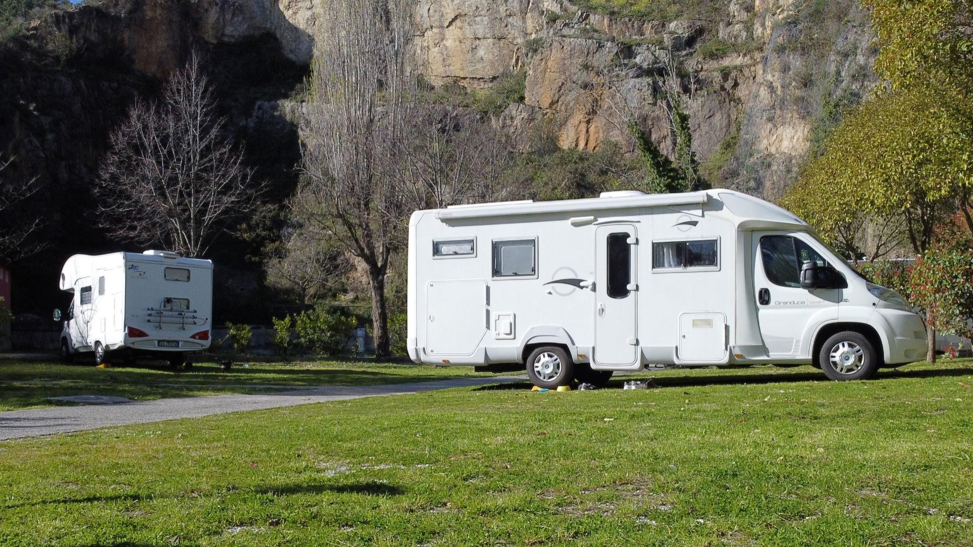 Two campers parked in a green area with a rocky cliff in the background.