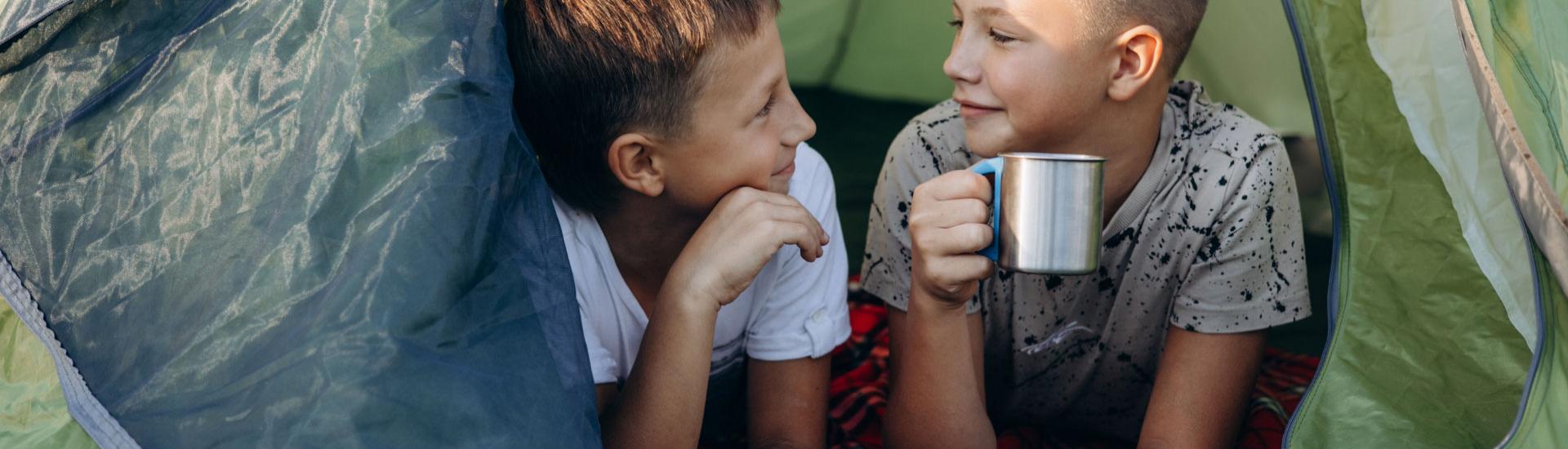 Due bambini in una tenda, uno beve da una tazza.