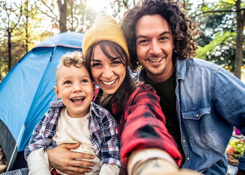 Happy family camping, smiling in front of the tent in the woods.