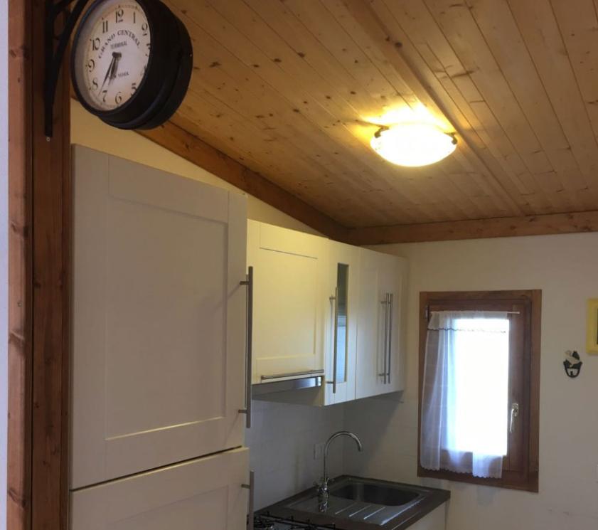 Small kitchen with wooden ceiling, vintage clock, and white cabinets.