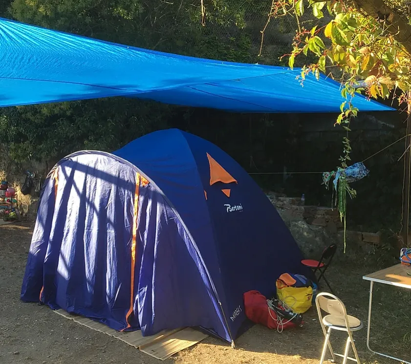Blue camping tent with a protective canopy in a wooded area.