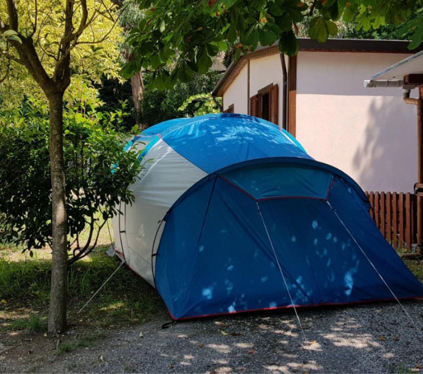 Tenda blu in campeggio vicino a una casa, circondata da alberi.