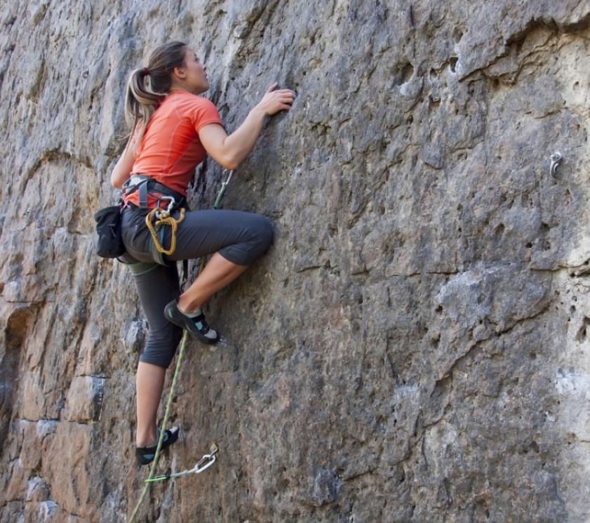 Person climbing a rock wall with climbing gear.