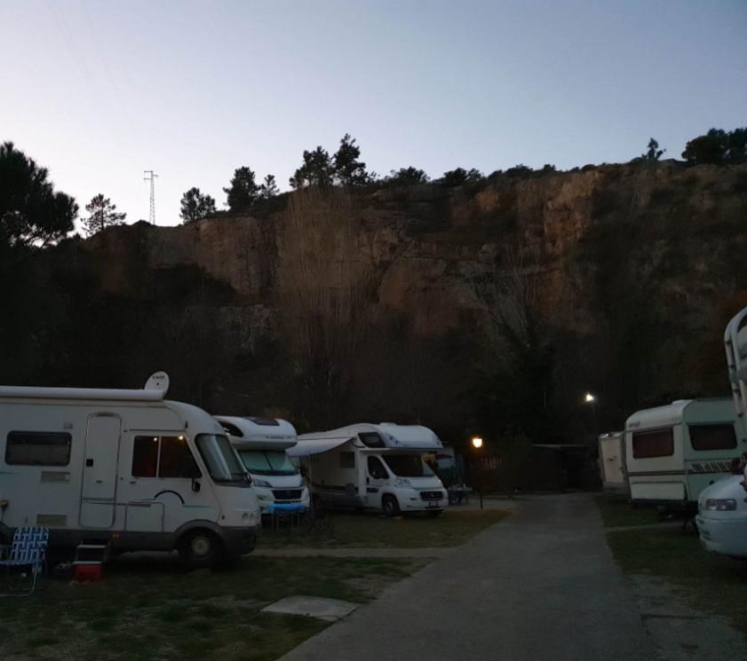 Camper vans parked in a rest area near a rocky cliff at sunset.