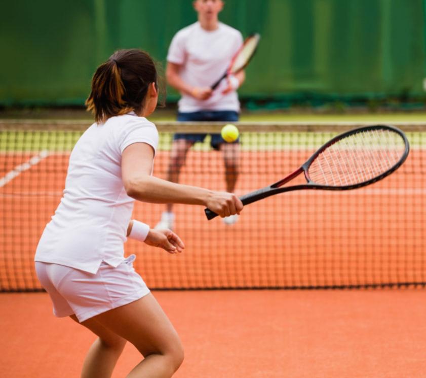 Due persone giocano a tennis su un campo con superficie arancione.