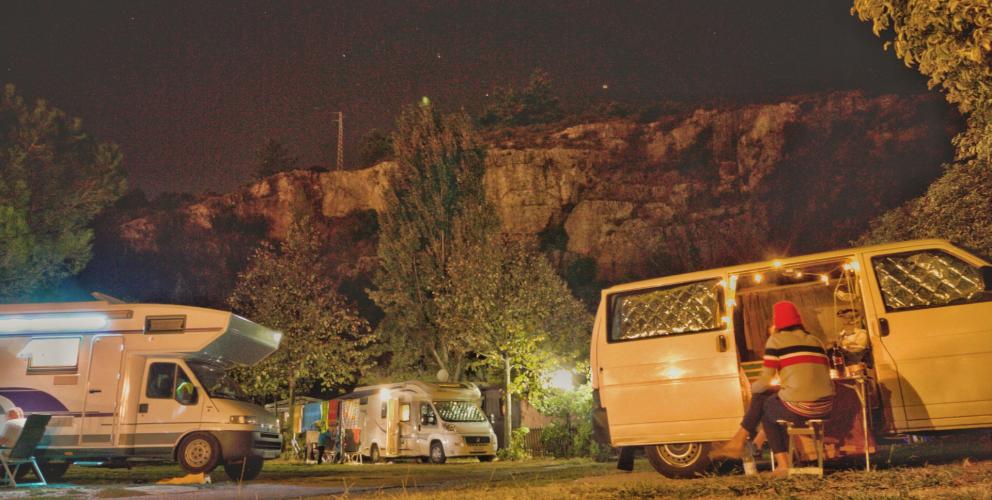 Campeggio notturno con camper e furgoni sotto un cielo stellato.